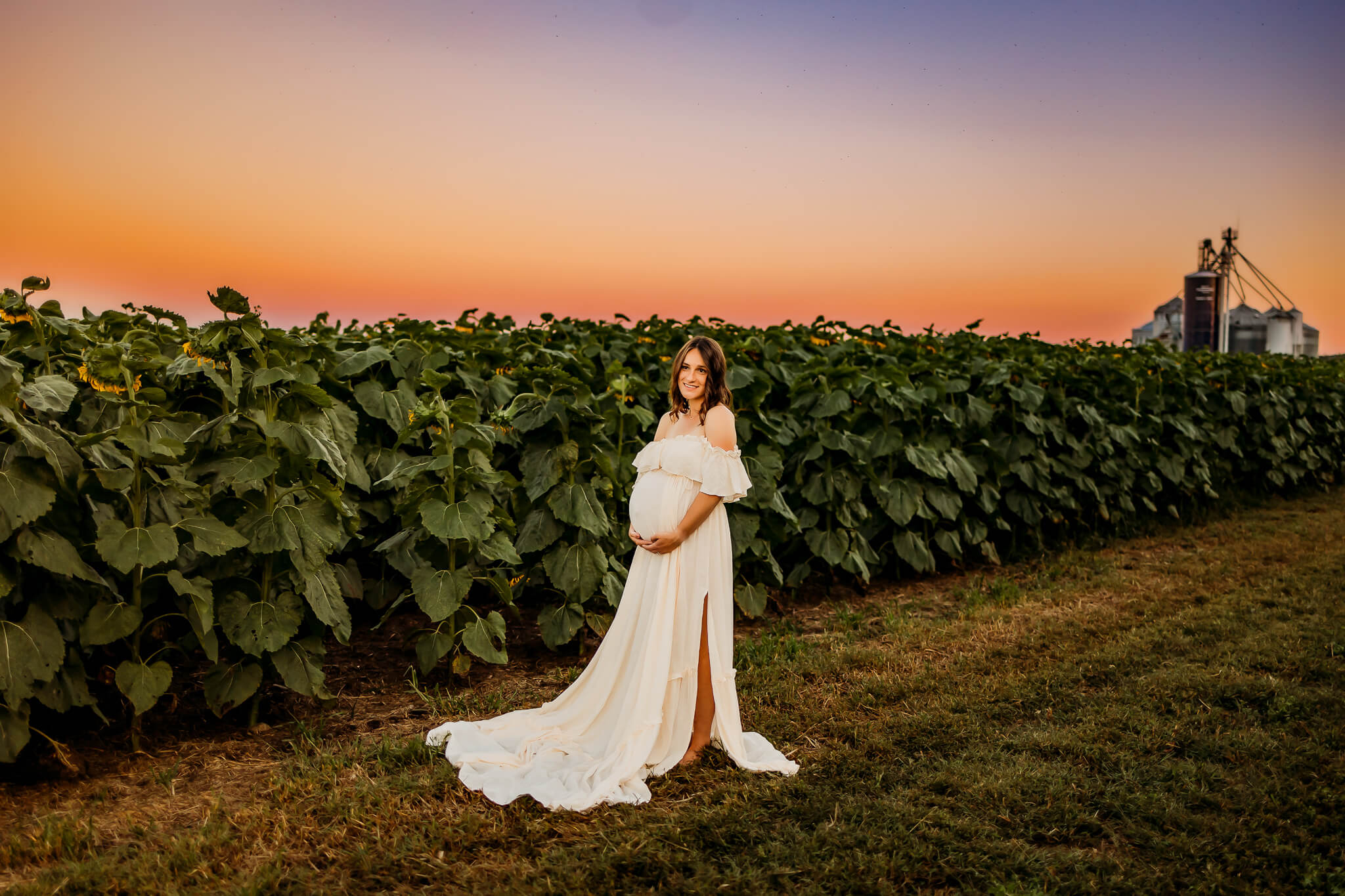 pregnant woman standing in a corn field while wearing a long white maternity gown Spas in Eau Claire