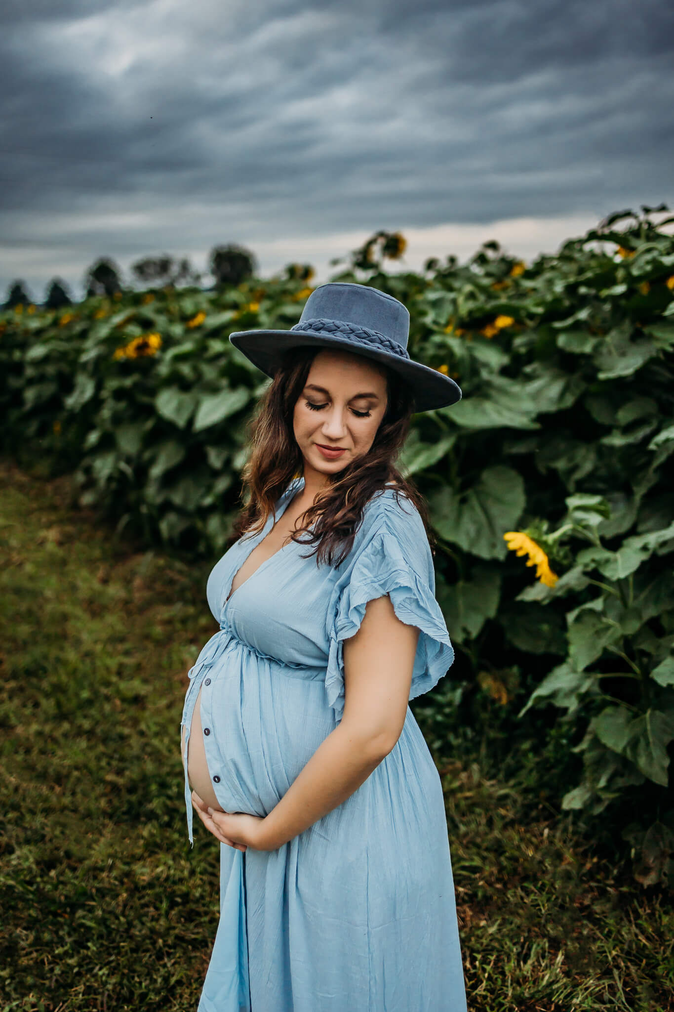 mom to be in blue maternity gown cradling her bump in a sunflower field doula eau claire wi