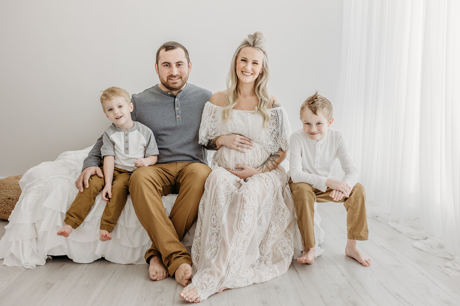 A family of four sits on a short bed while mom places both hands on her pregnant belly eau claire chiropractors