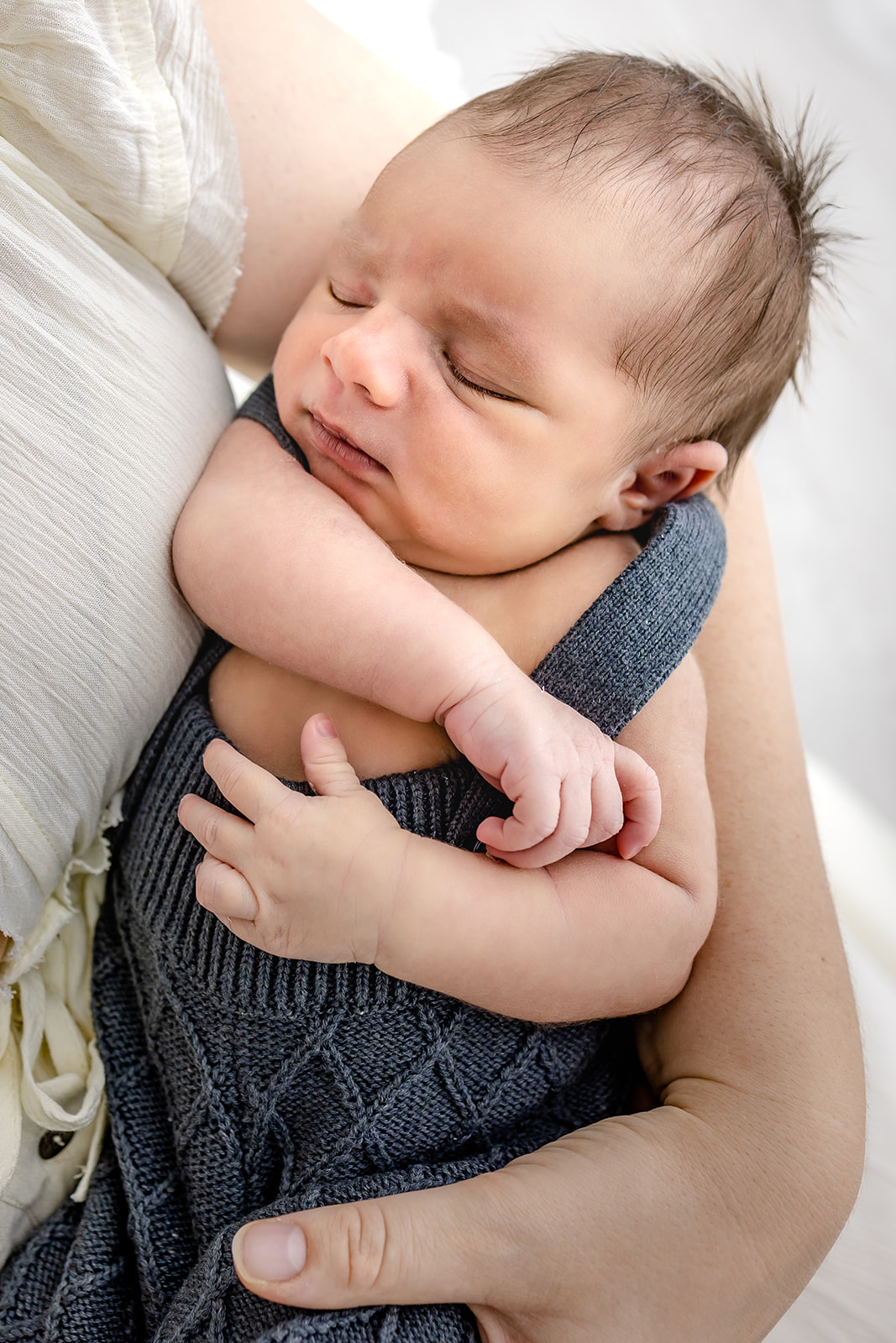 A newborn baby in a blue onesie sleeps in mom's arms