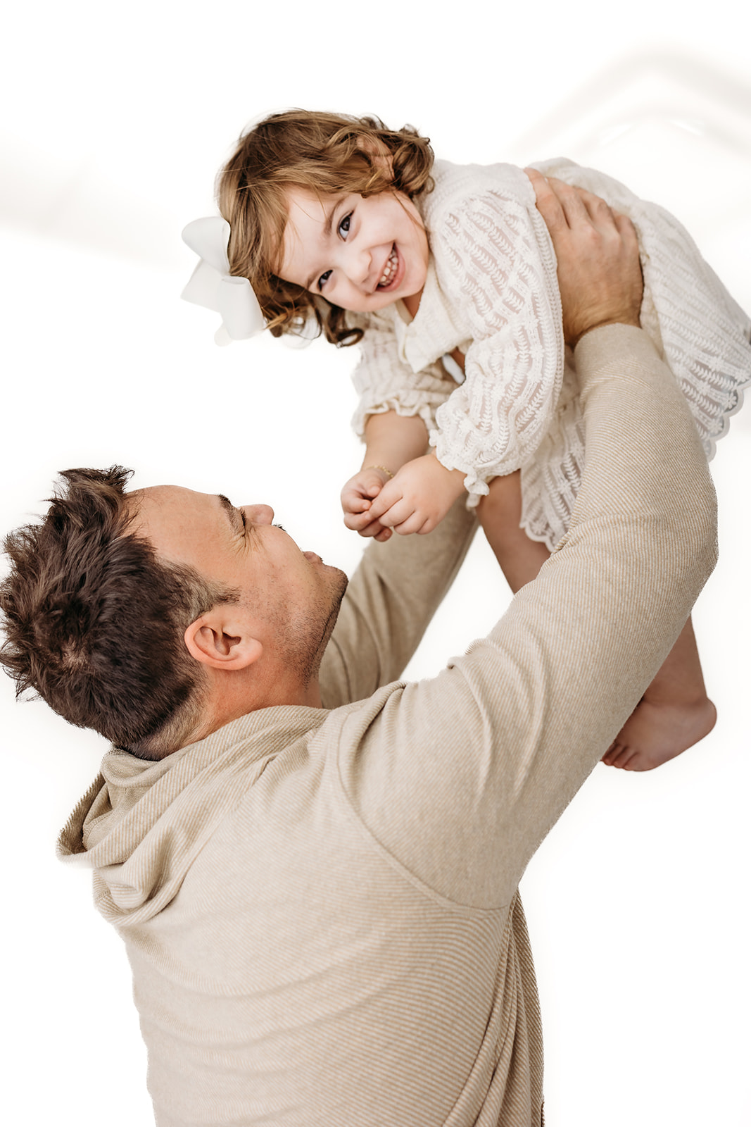 A happy dad lifts and plays with his toddler daughter in a studio after visiting Eau Claire Preschools