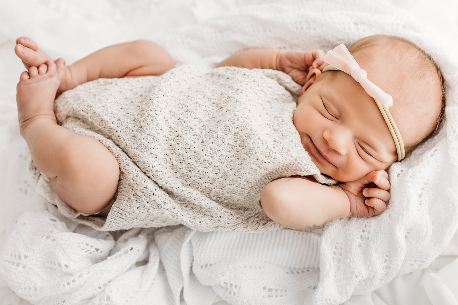 A newborn baby smiles in her sleep on a lace blanket in a knit onesie thanks to Beautiful Birth Doula