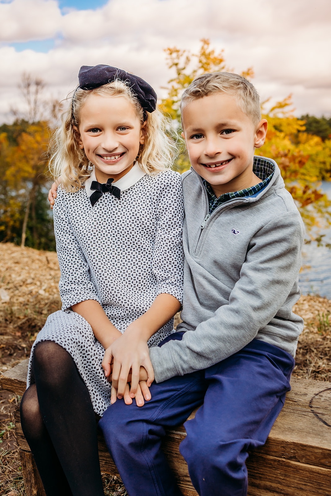A young brother and sister sit together on a lakeside park bench in fall holding hands after attending Montessori School Eau Claire