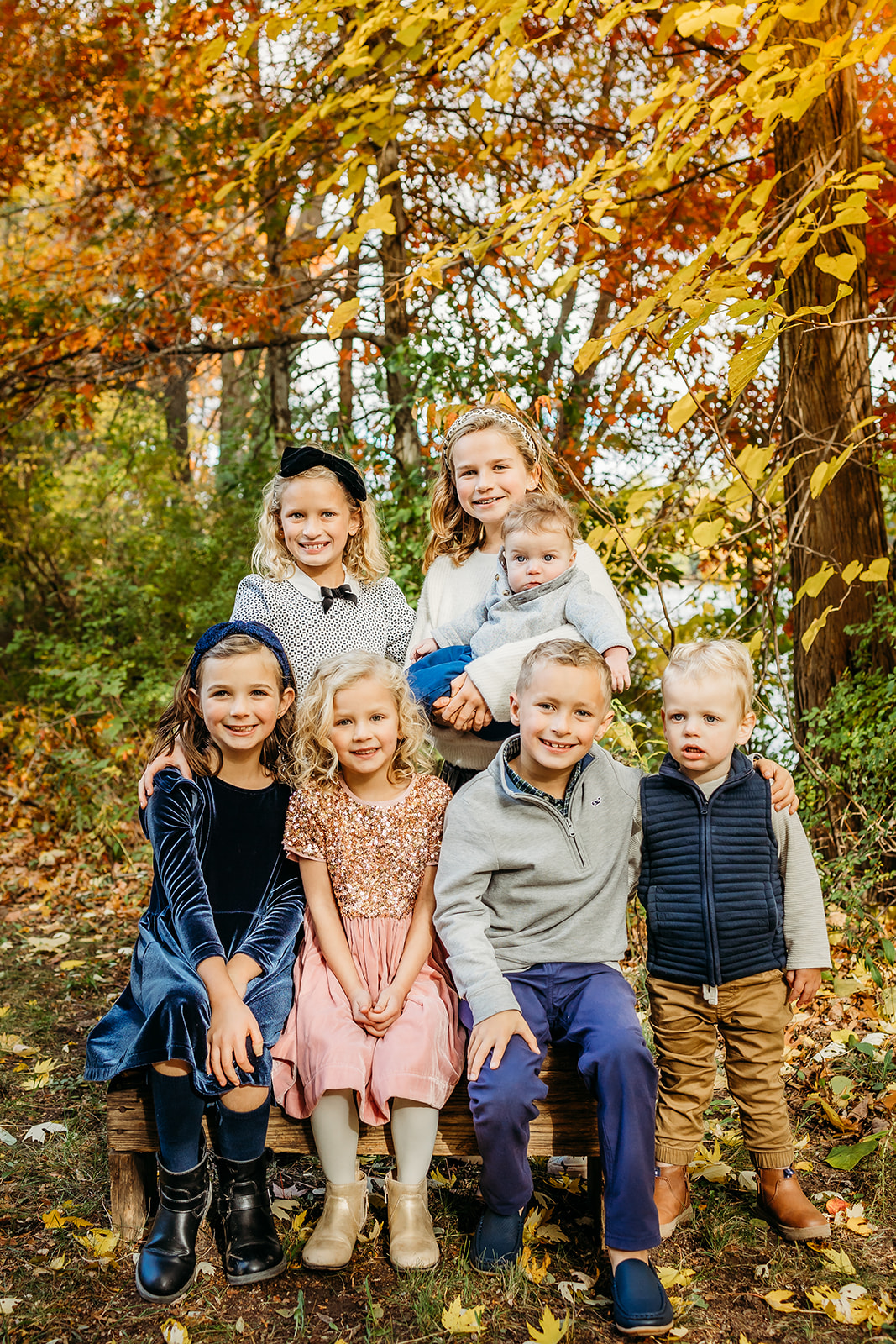Seven siblings sit together on a park bench in a park in fall after attending Montessori School Eau Claire