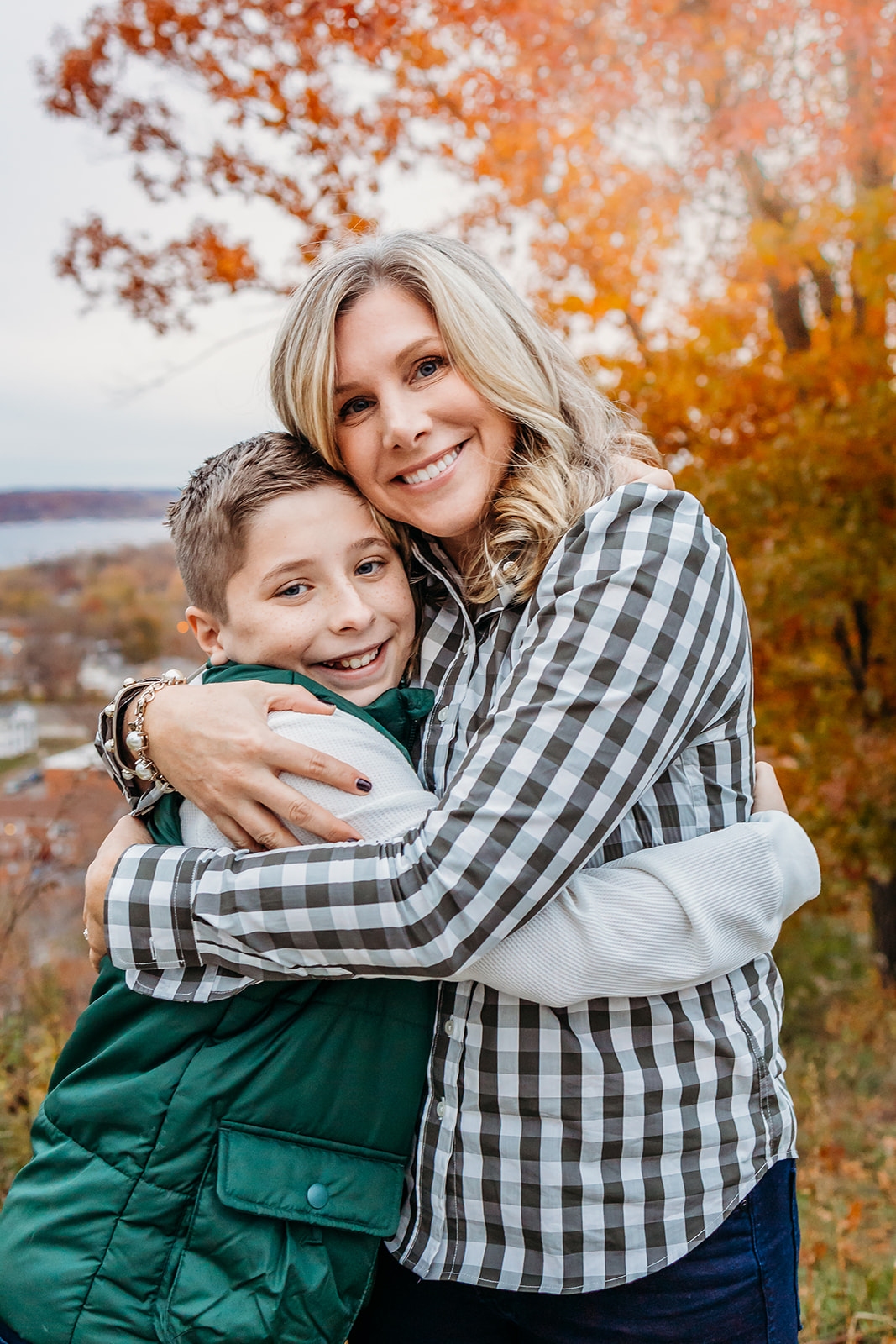 A mother hugs her young son while standing in a hillside park in fall